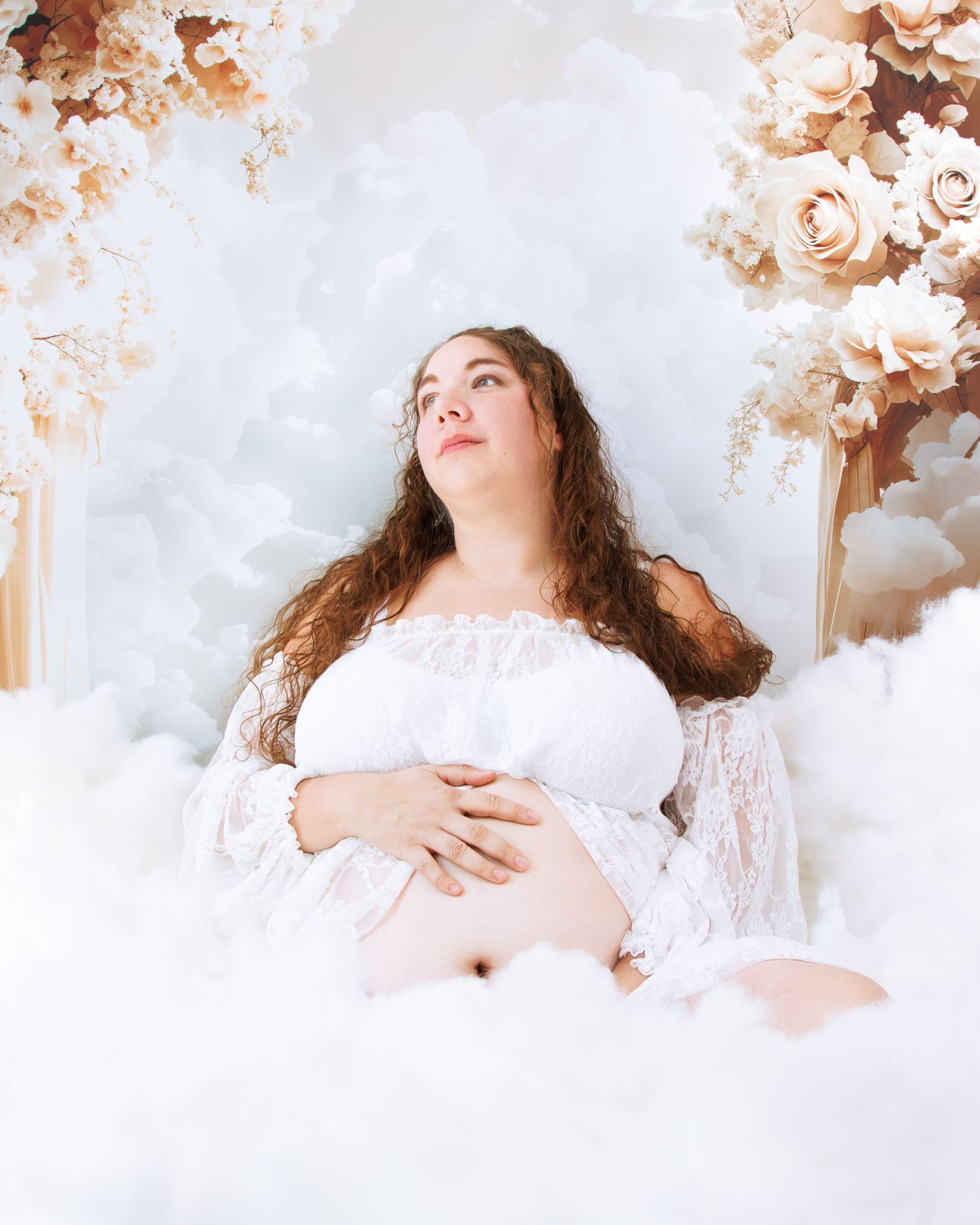 Elegant maternity portrait with roses and cloud-like decor in soft lighting.