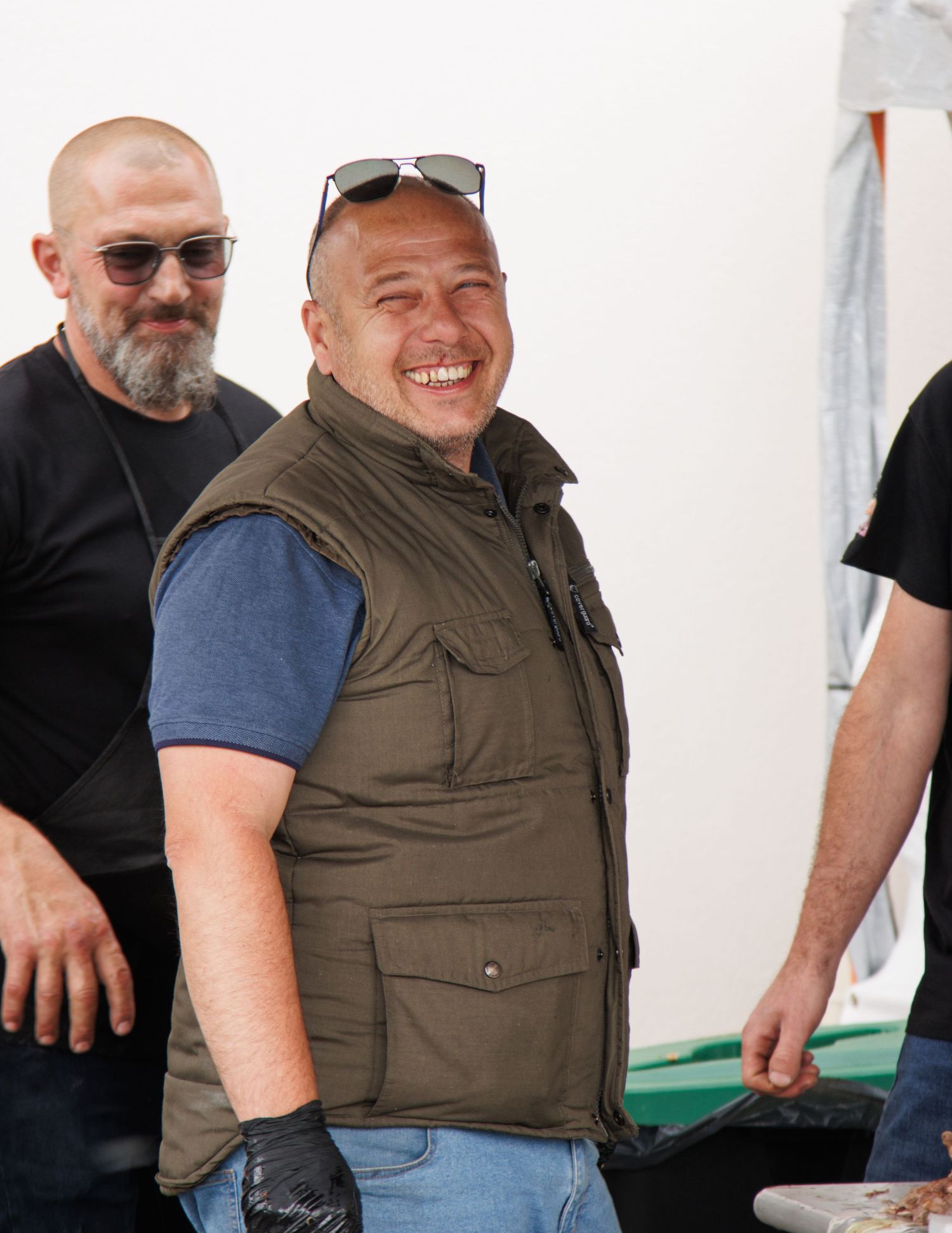 People in casual attire and vests standing together during an outdoor gathering.