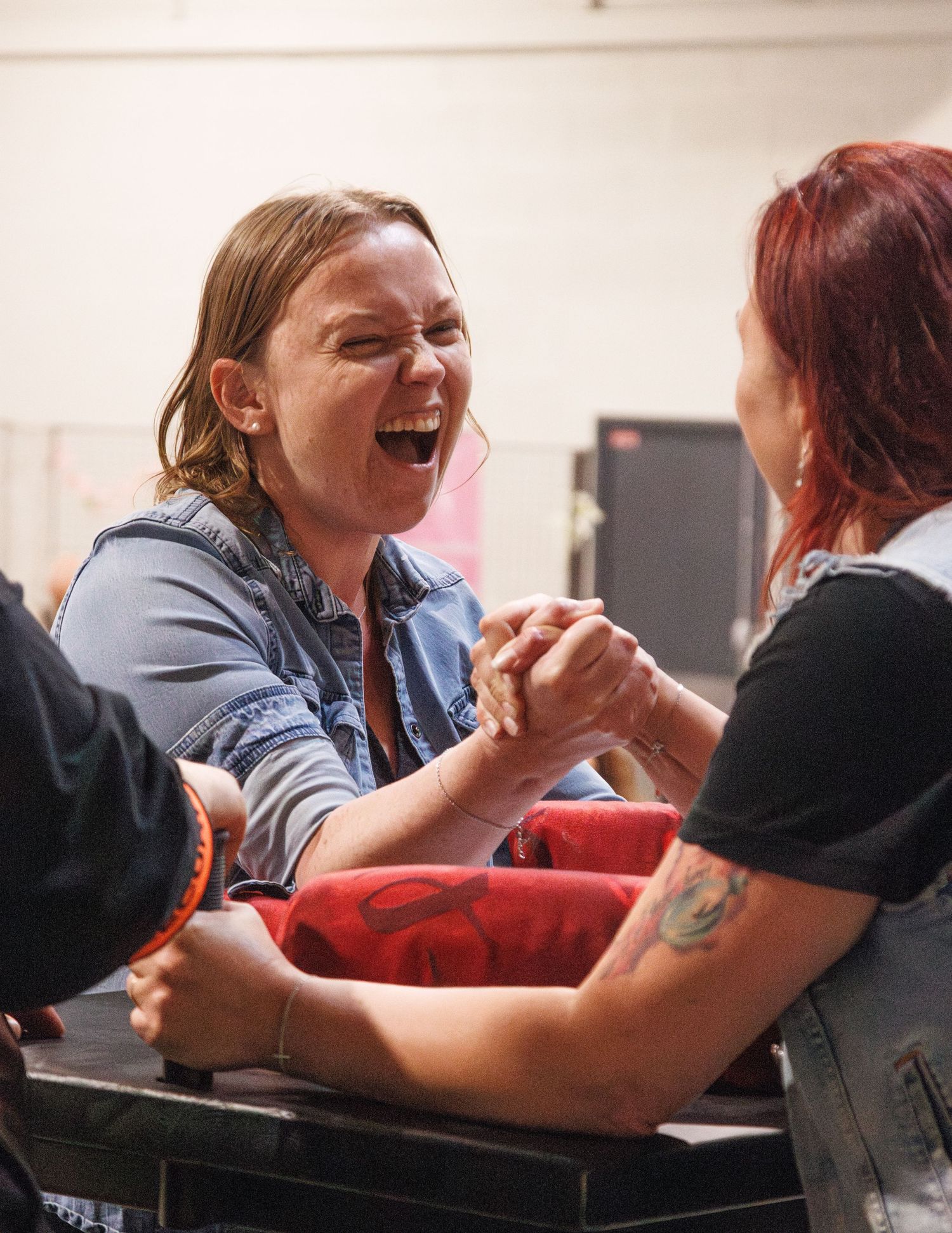 Two people laughing during competitive arm wrestling match at indoor event.
