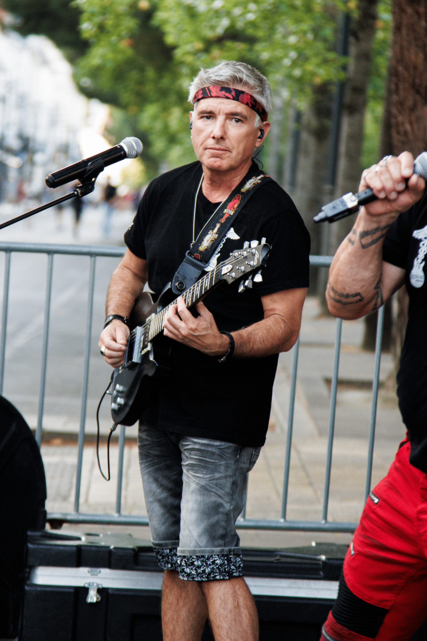 Guitar player wearing bandana performs at outdoor concert behind metal barrier.