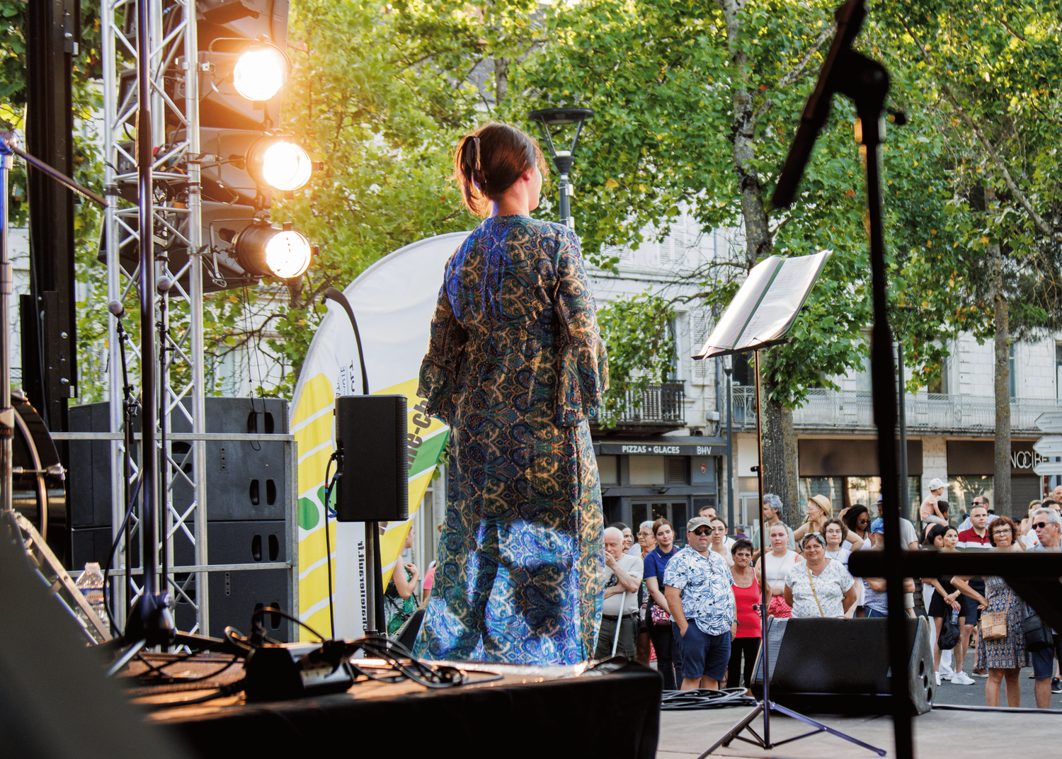 Outdoor concert stage with lighting equipment and trees visible in background.