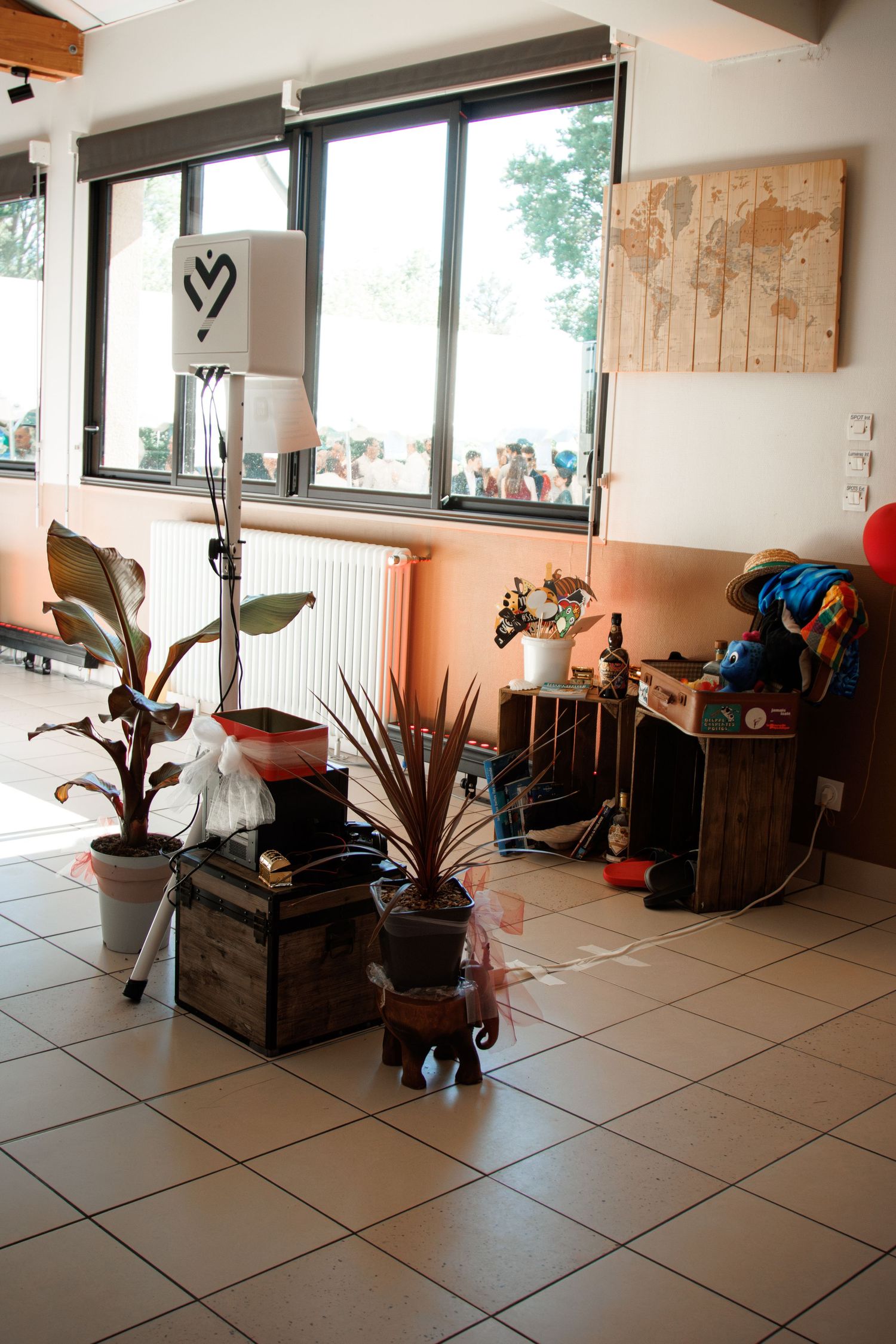 Indoor wedding venue corner with tropical plants, wooden crates, world map decor and heart sign.