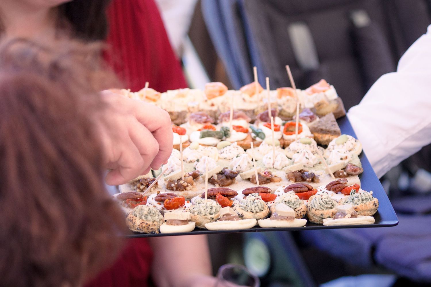 Wedding guests selecting assorted canapes from a catering tray at a reception cocktail hour.