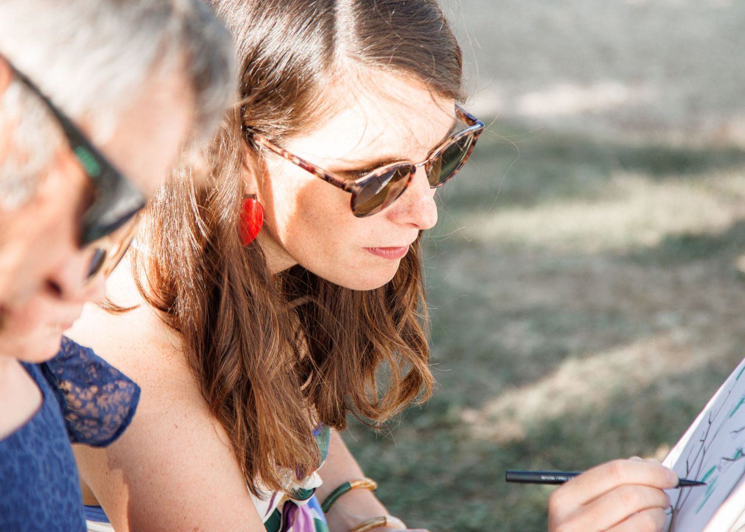 Wedding party members gather outdoors in casual summer attire under sunlit natural surroundings.