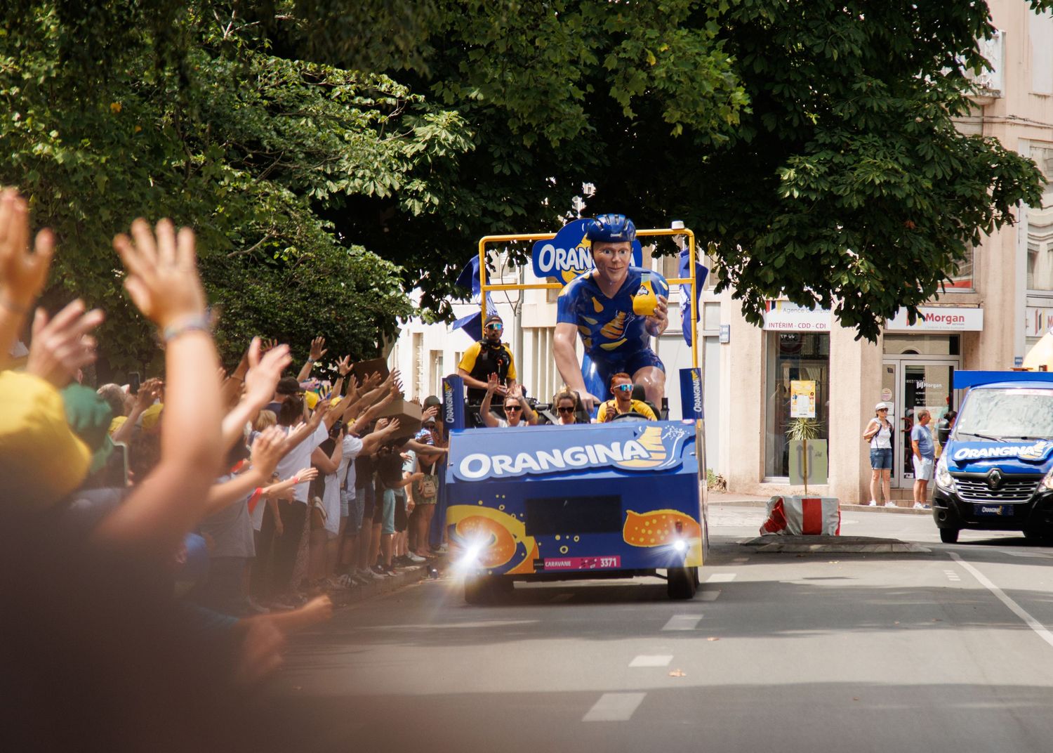 A promotional float driving through streets as crowds wave and cheer.