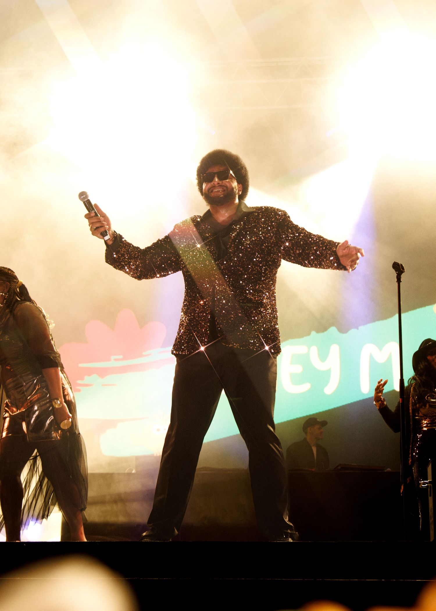 Performers in sequined outfits dance energetically on a backlit stage with dramatic lighting effects.