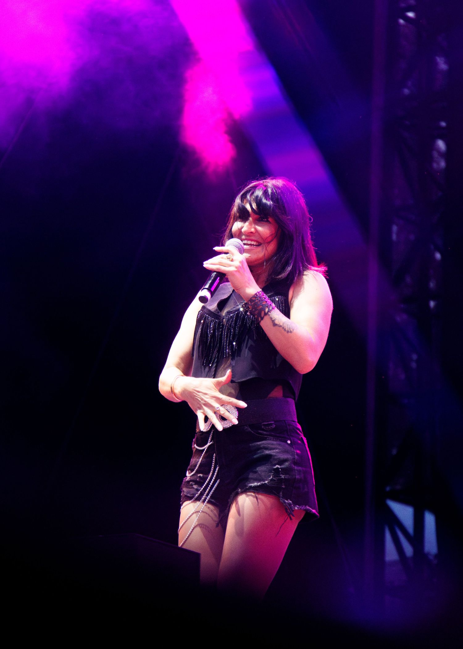 Performer in black outfit dances on stage with vibrant pink and purple lighting effects in the background.