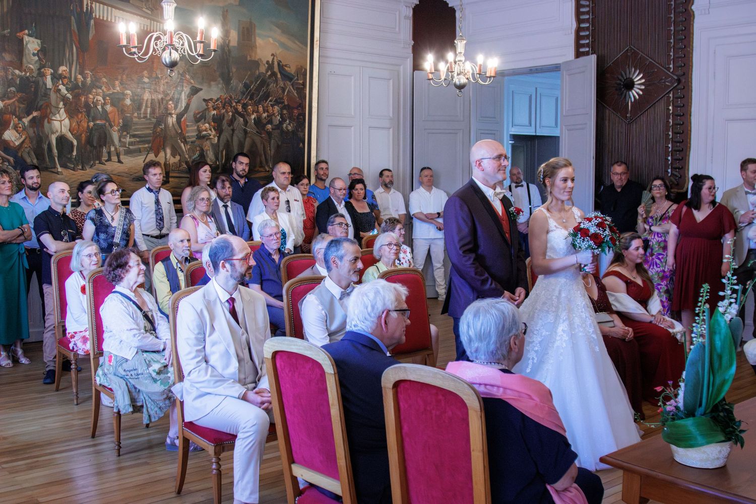 Bride in white gown walks down aisle with escort during formal wedding ceremony.