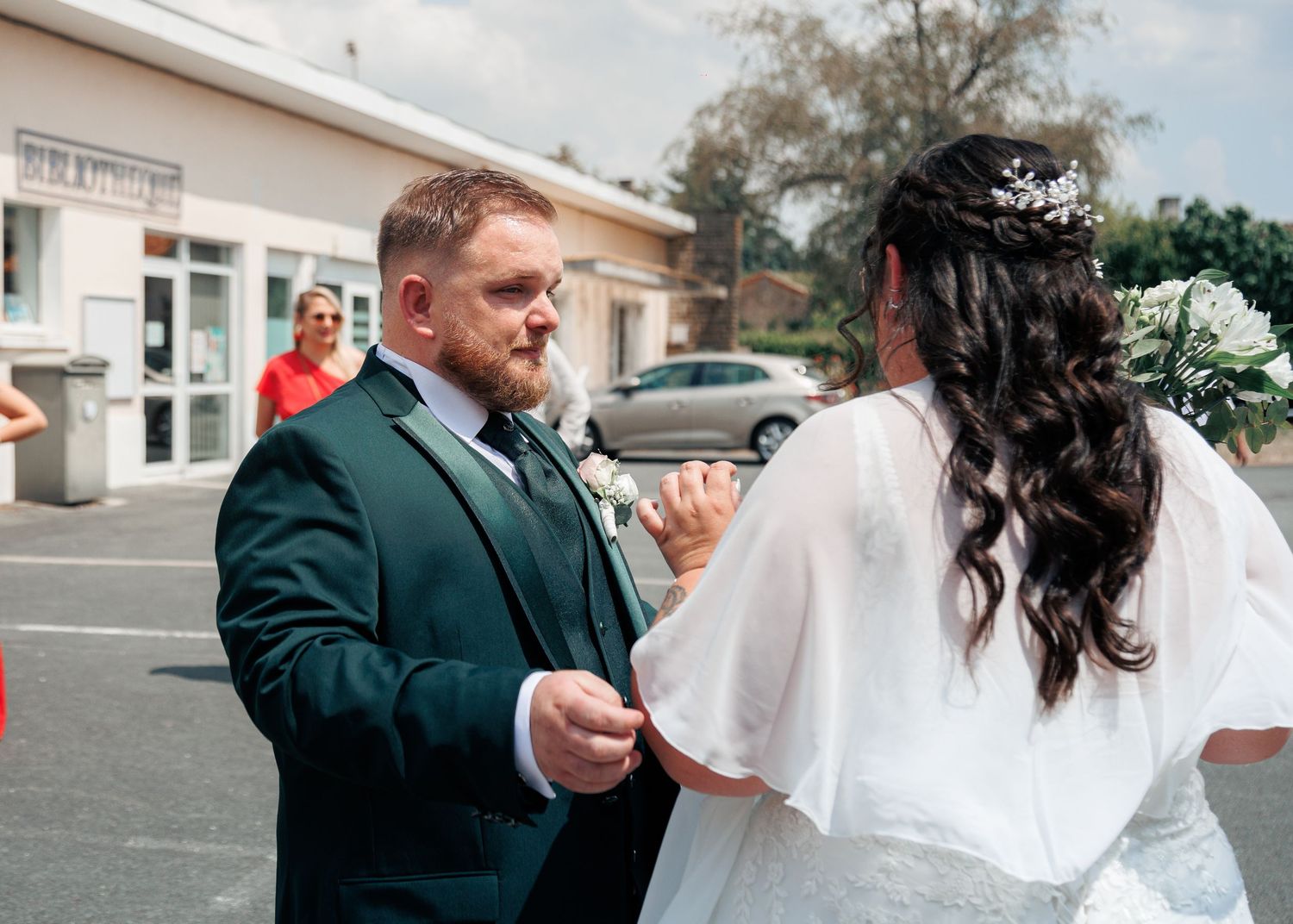 A groom in a dark green suit shares a tender moment with his bride in a white dress outdoors.