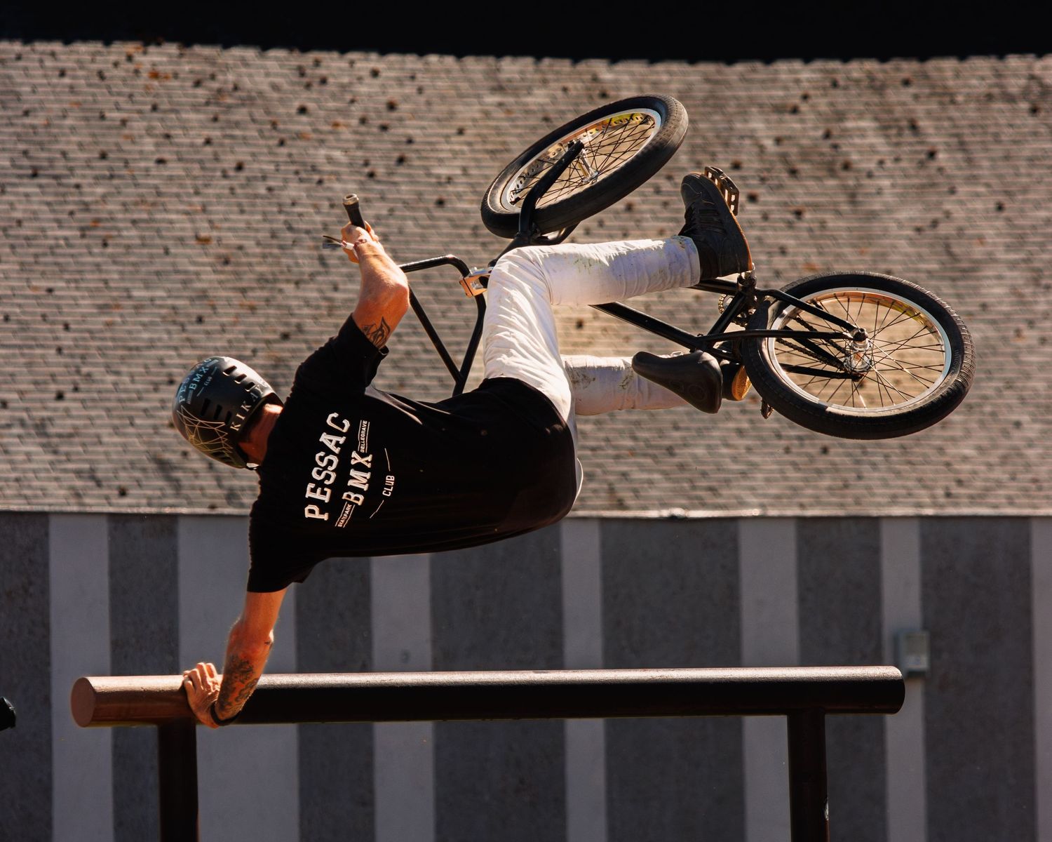 BMX rider executing horizontal spin trick over metal rail in urban setting.