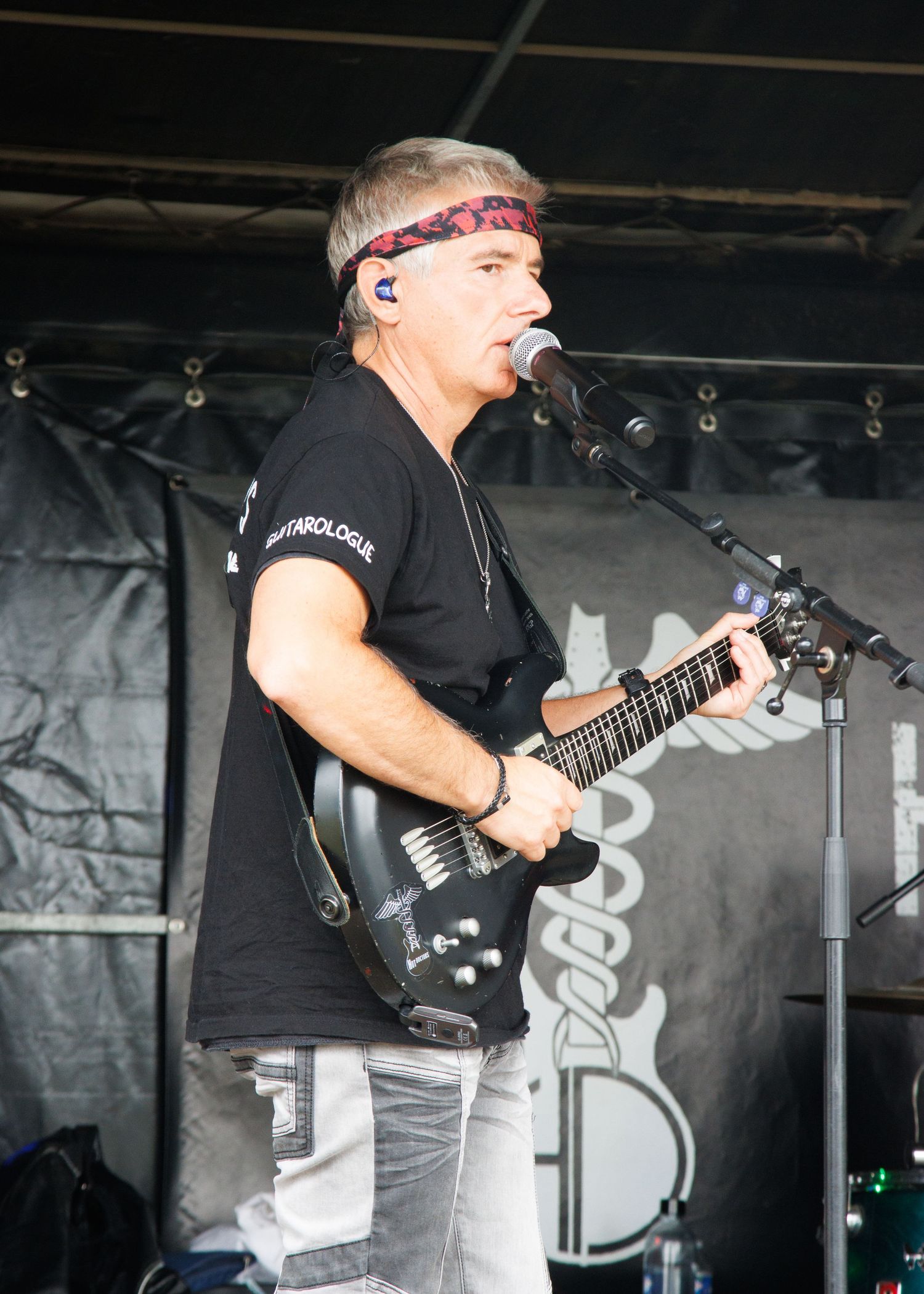 Musician wearing bandana performs with guitar on stage with black backdrop.