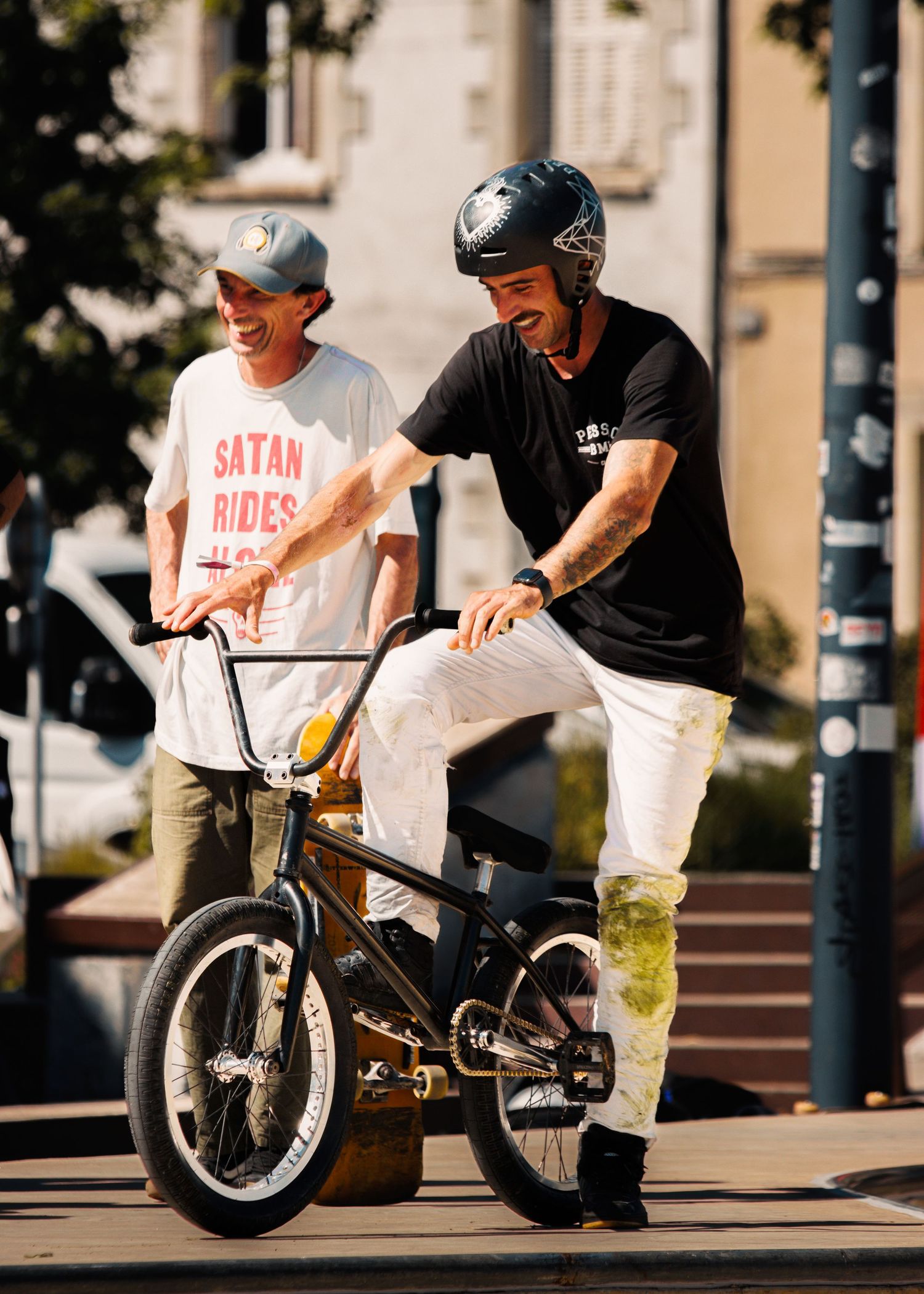 BMX riders gather and practice tricks in urban plaza setting.