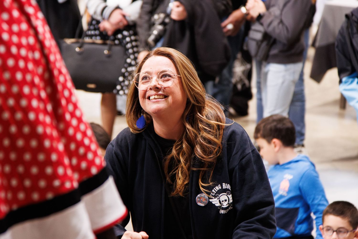 Person in a black sweatshirt smiling during an indoor event with a crowd in the background.