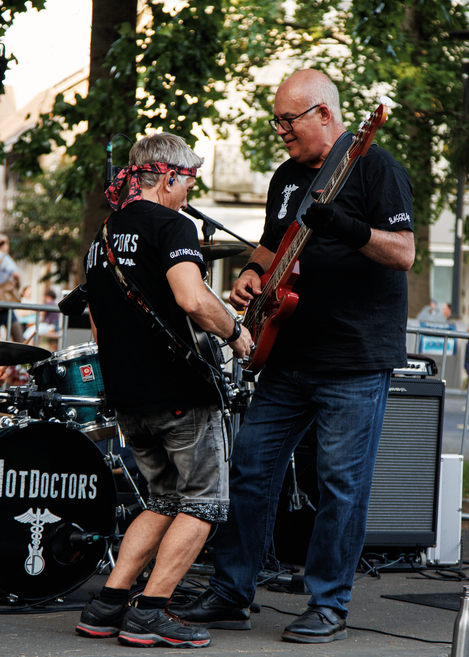 Two musicians playing guitars together on outdoor stage with band equipment.