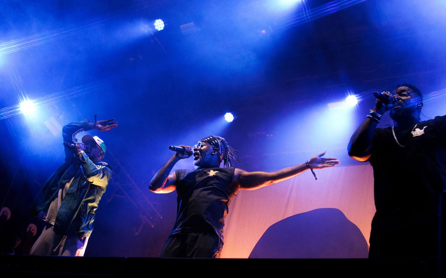 Silhouetted performers on stage with dramatic blue lighting and fog effects during a concert performance.