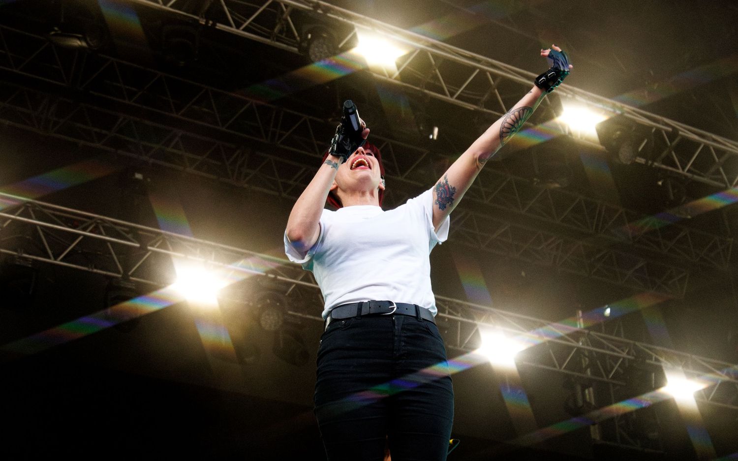 Person in white shirt raises fist triumphantly on stage under bright spotlights at live concert event.