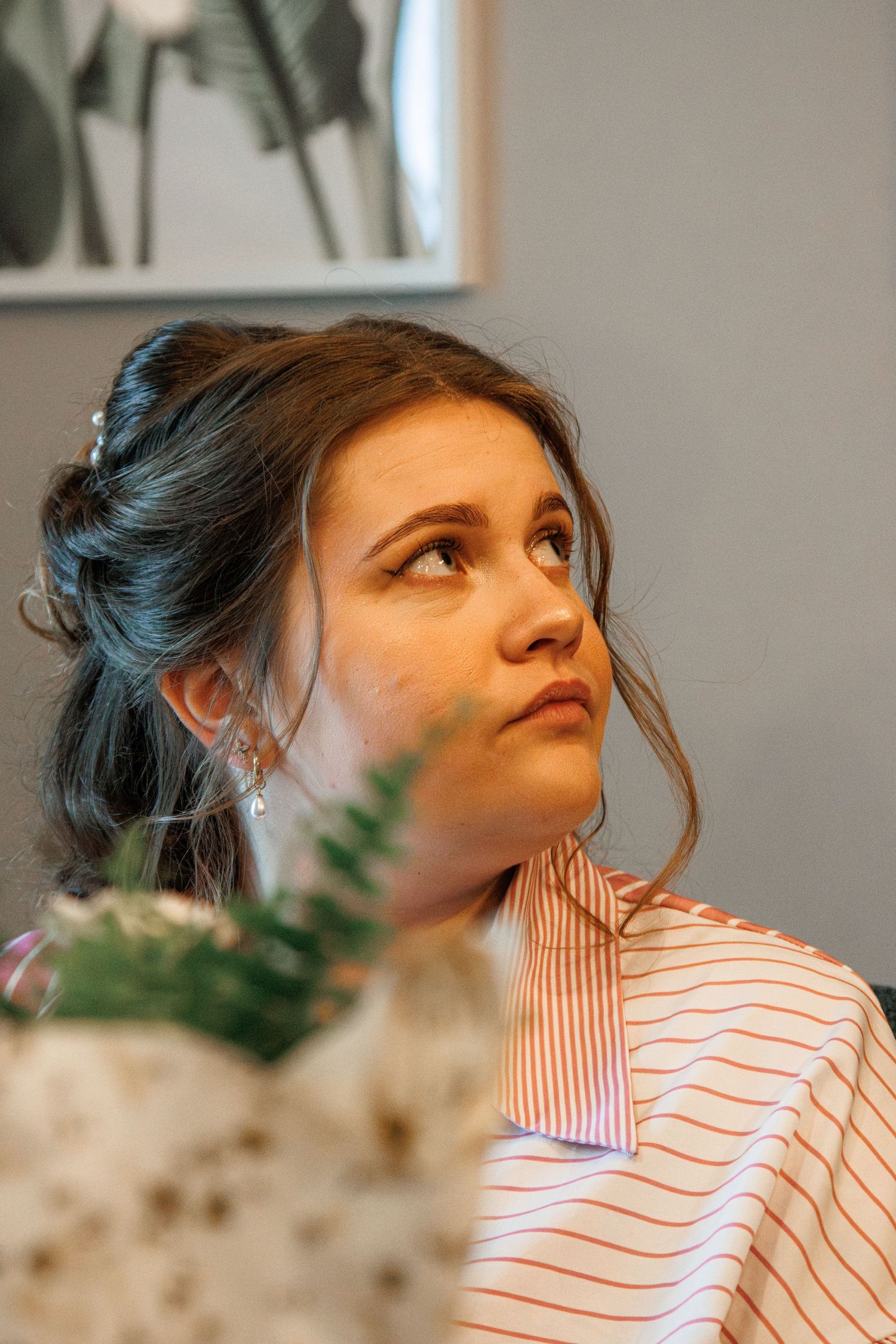 Young woman with elegant updo hairstyle and drop earrings gazing upward, wearing a striped top in a salon setting.