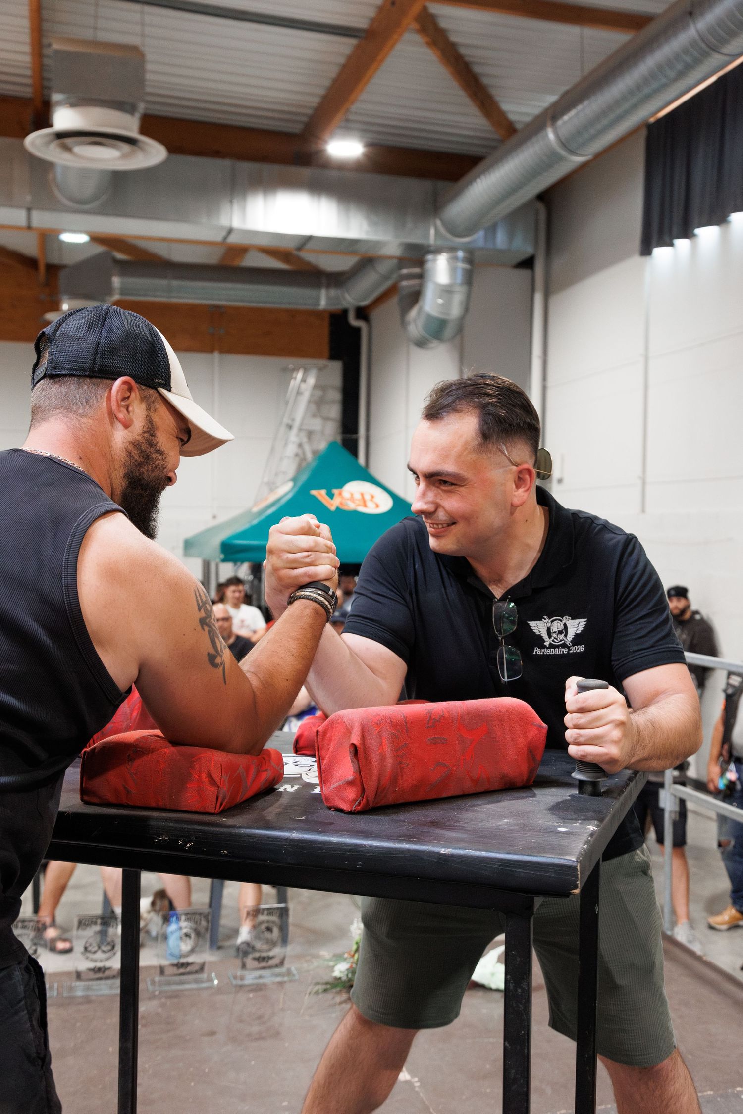 Two men arm wrestling at a table during a competition event held indoors at a large venue.