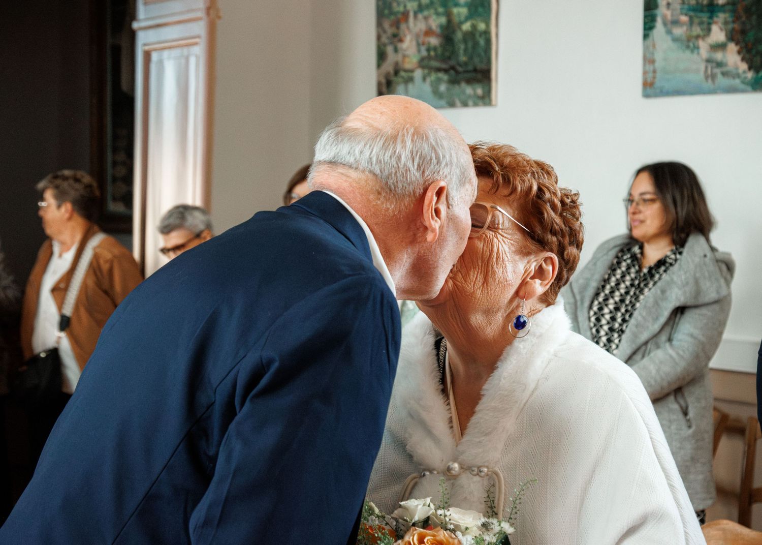 Elderly couple sharing a tender kiss at a wedding reception indoors.