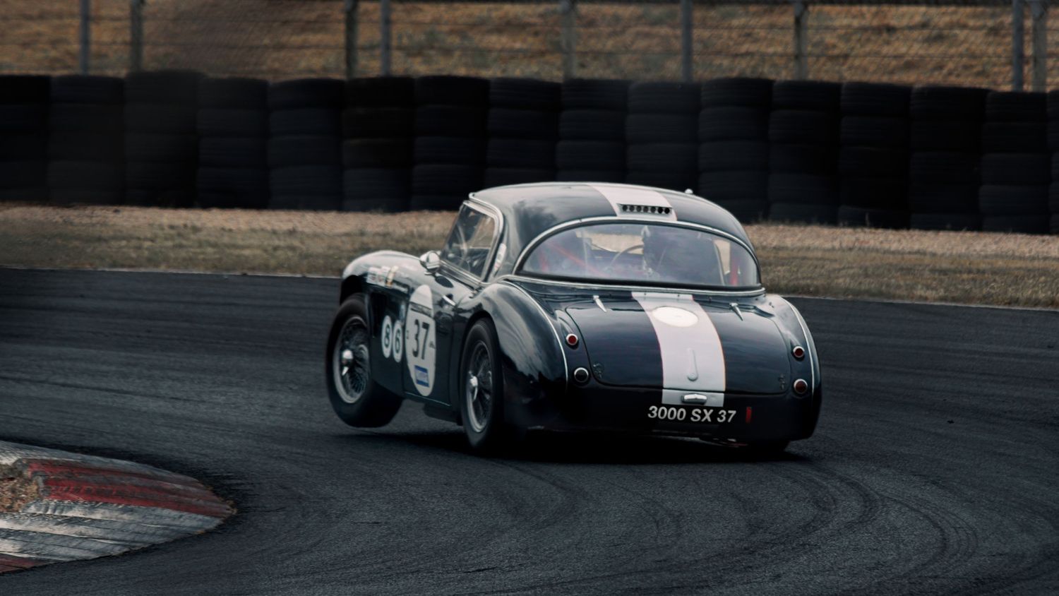 Historic racing cars navigate a tight corner on a professional racing circuit.