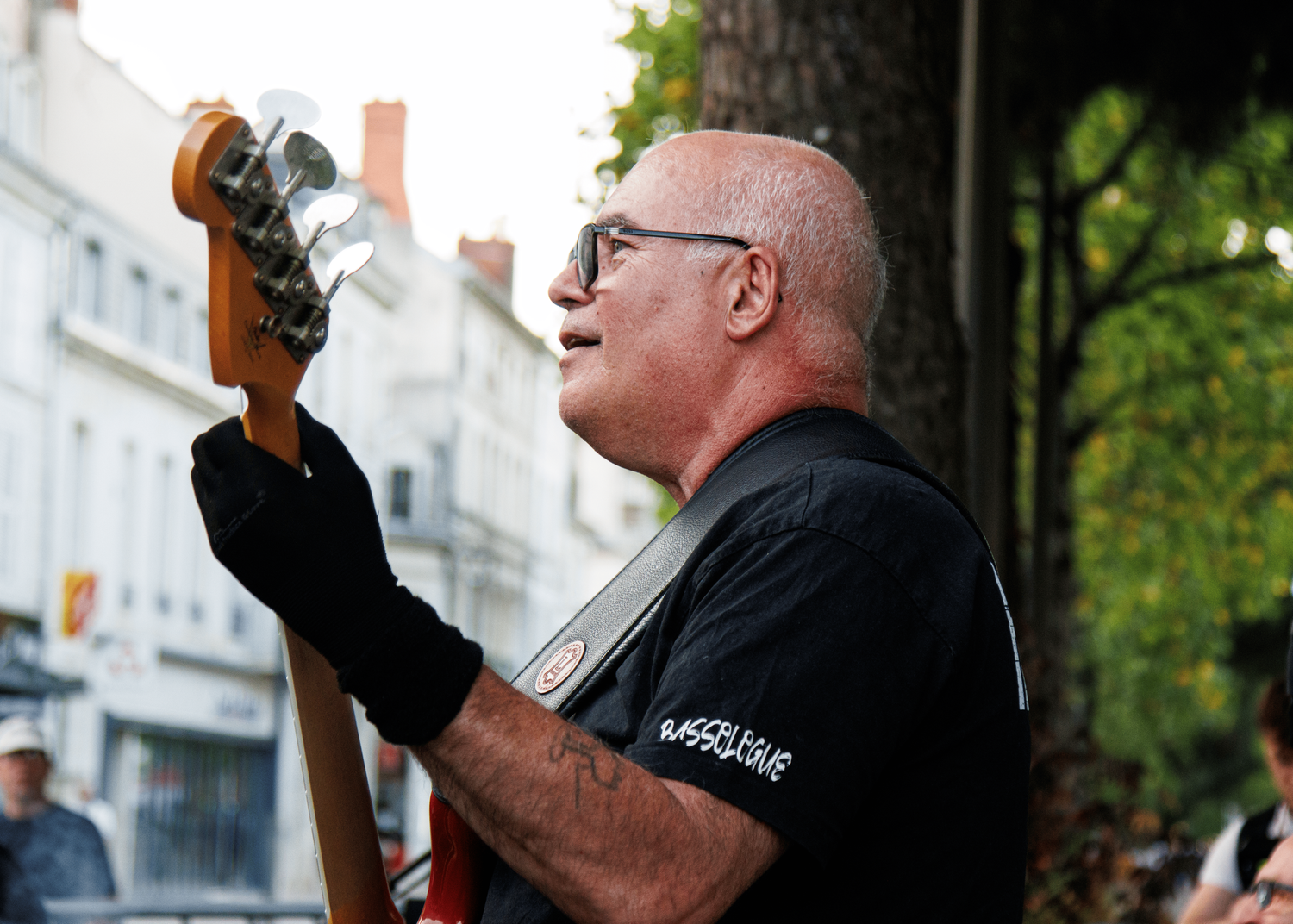 Bass guitarist performing outdoors while wearing glasses and black shirt.