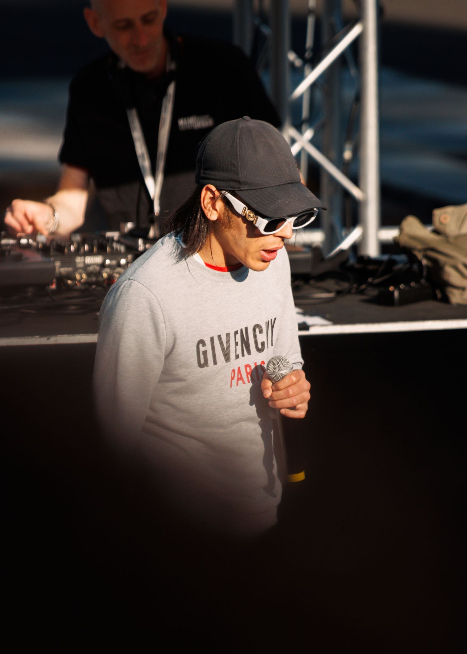 Performer in Givenchy sweatshirt and cap at outdoor event.