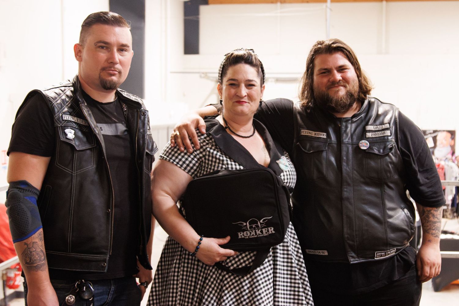 Group of leather-clad bikers gathered for a photo in a light indoor setting.