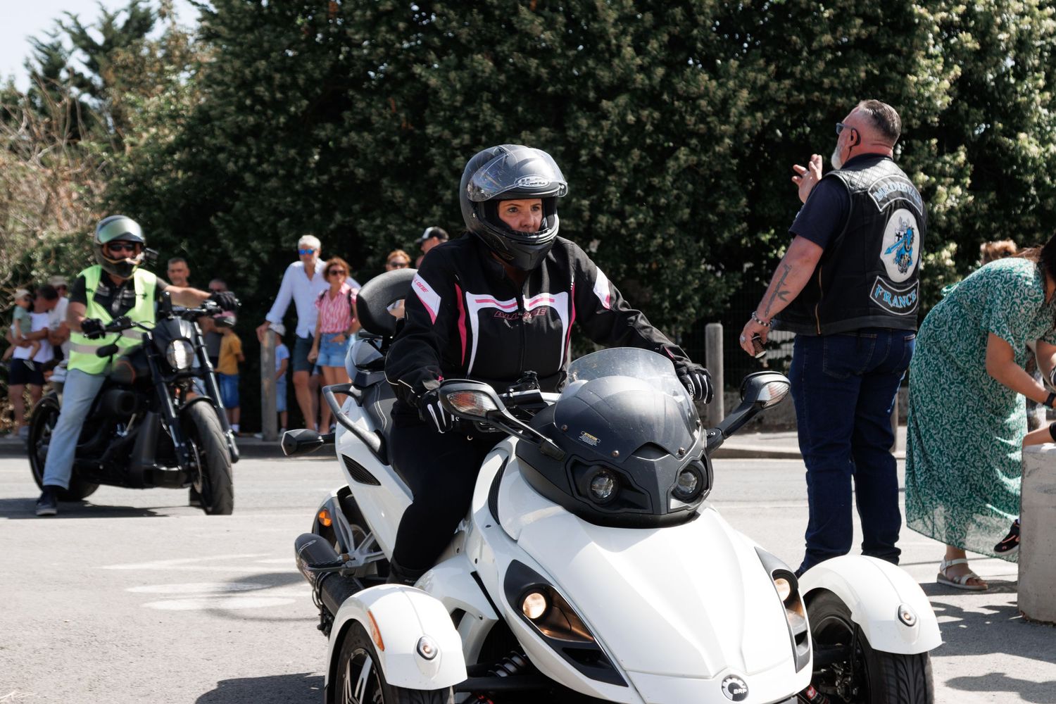A motorcyclist in a black helmet rides a white three-wheel Can-Am trike during an outdoor motorcycle rally event.