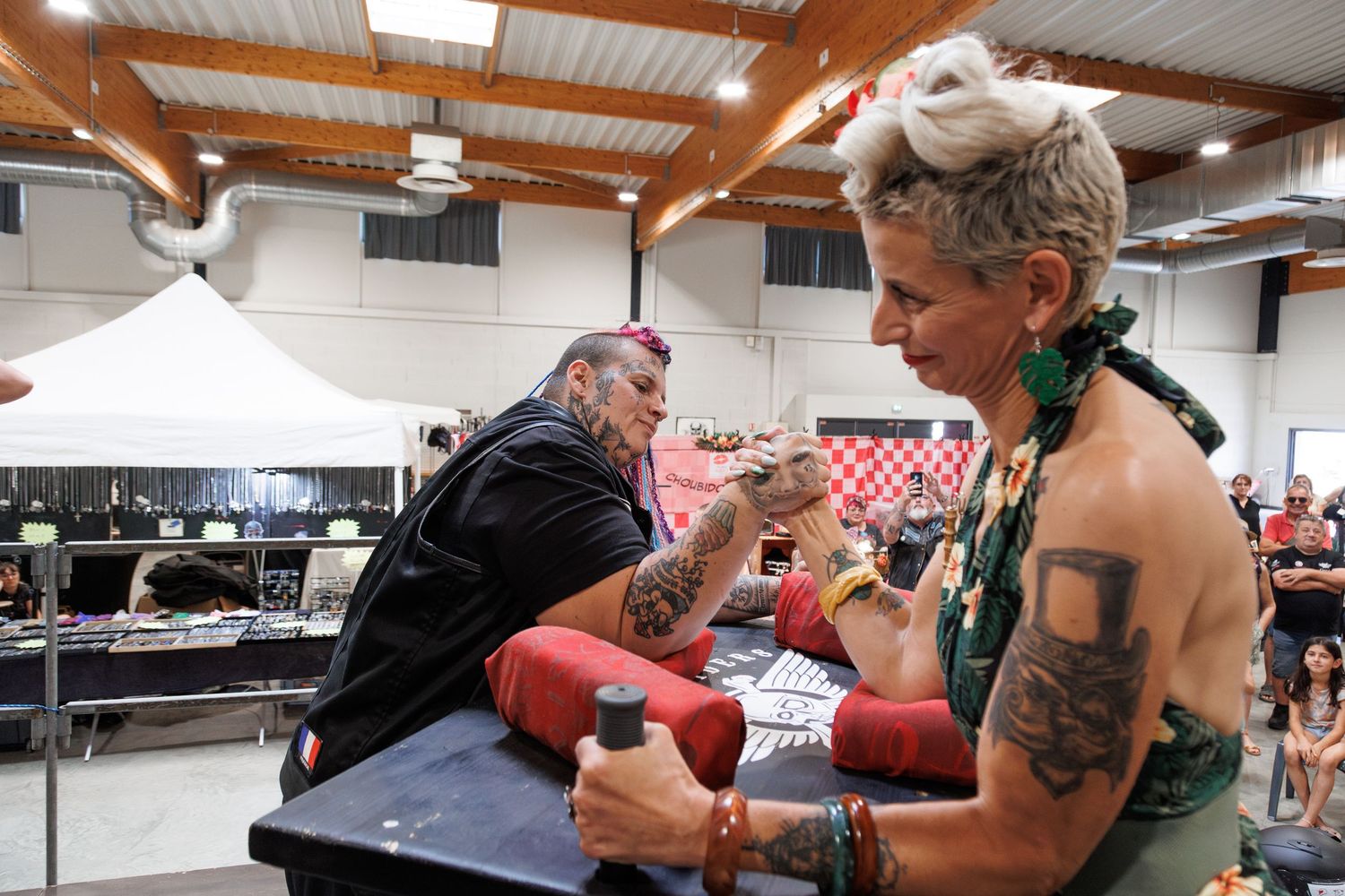 Tattoo artist inking a heavily tattooed person at an indoor tattoo convention event.