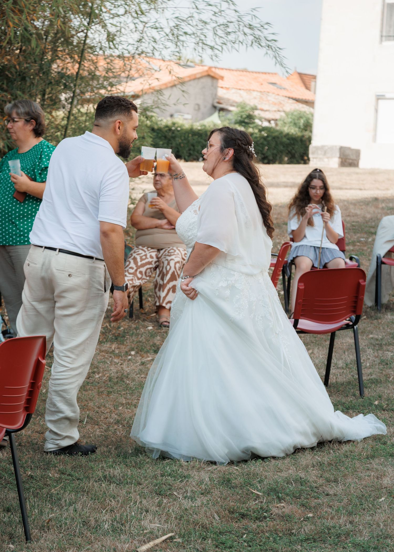 Bride in white tulle gown dances joyfully with guest in white shirt at outdoor wedding reception.