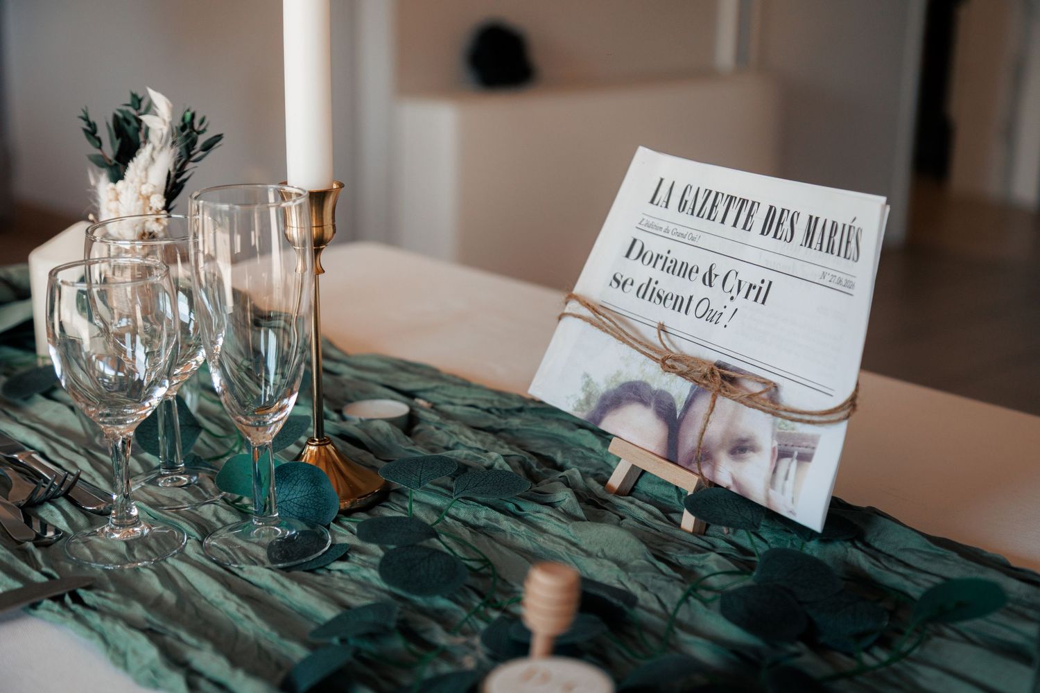 Wedding table decor with green runner, candles, wine glasses, and La Gazette des Maries newspaper.