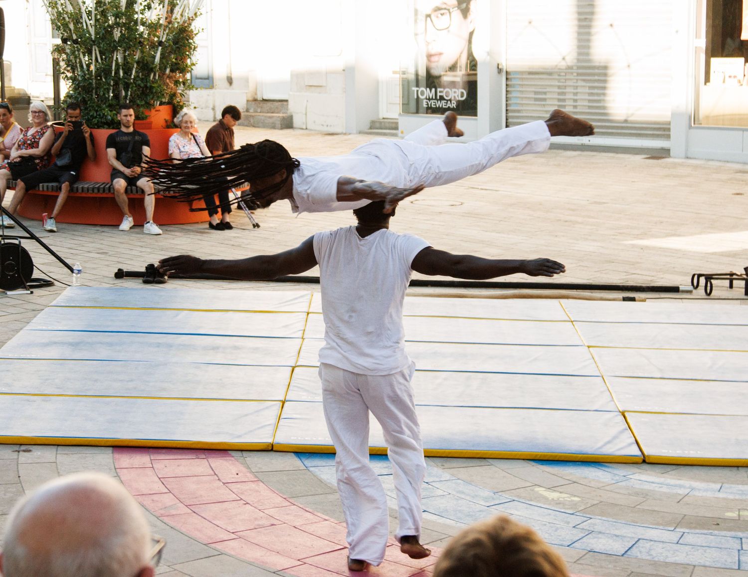Performer in white demonstrates a horizontal balance pose during outdoor street show.