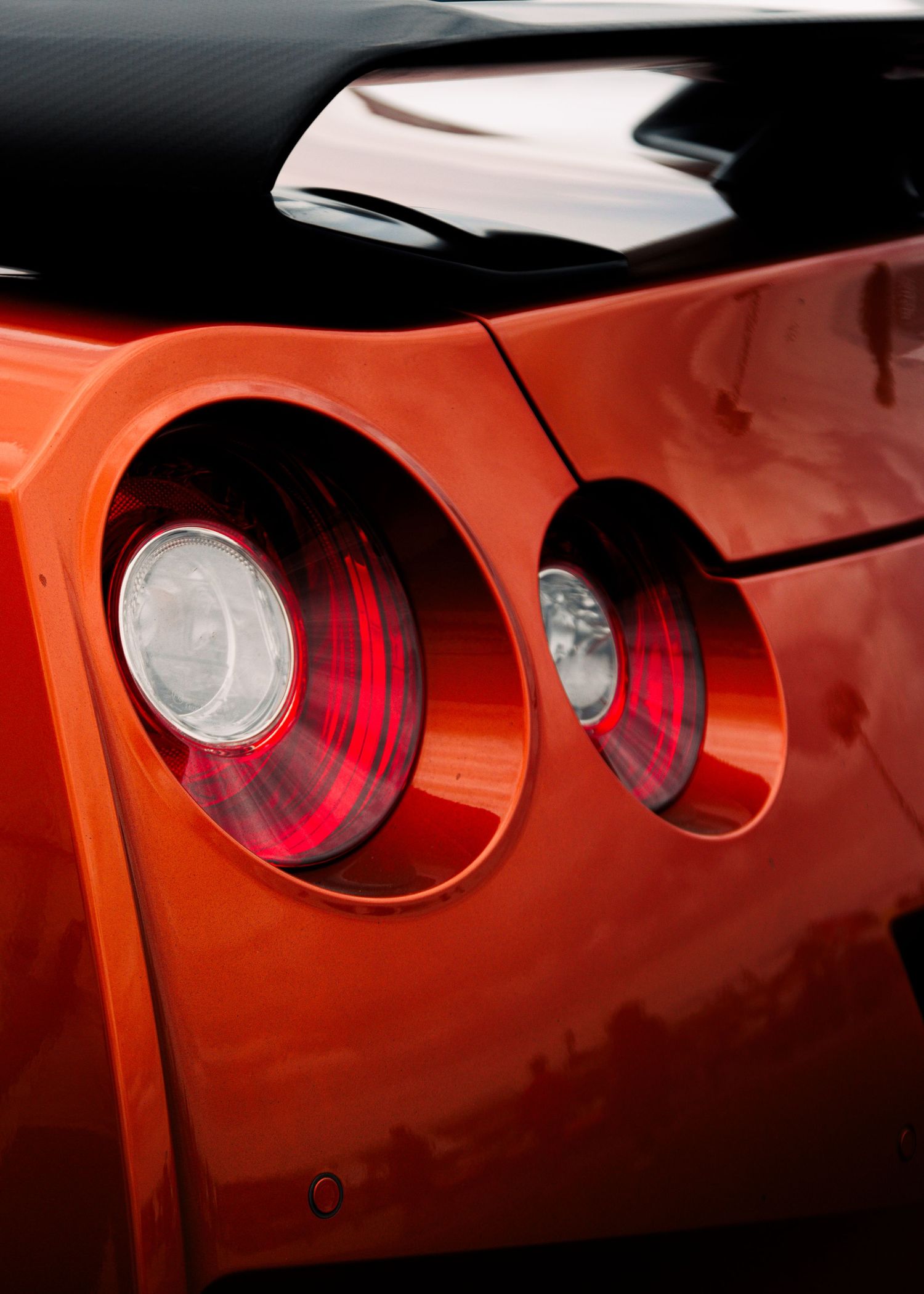 Row of distinctive red circular taillights on an orange sports car body panel.