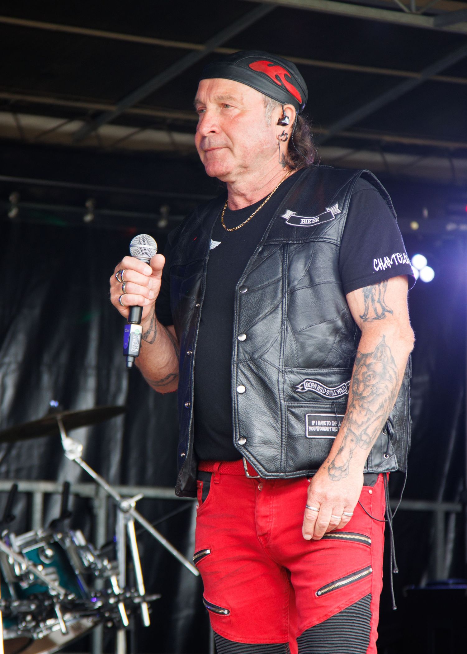 Performer in leather vest and red pants singing on stage with microphone during concert performance.