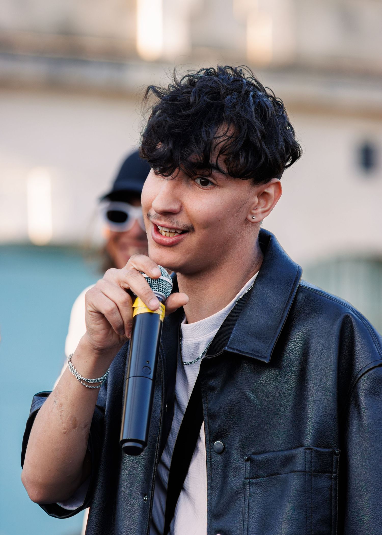 Person in black leather jacket holds microphone while smiling.
