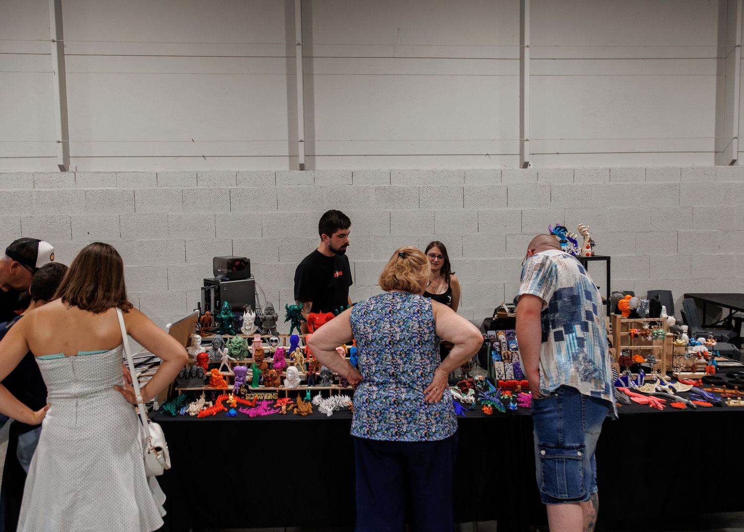 People browsing colorful items at an indoor vendor table during a convention or flea market event.