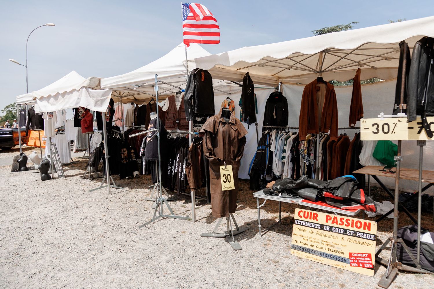 Outdoor flea market stall selling leather jackets and clothing under white tents with an American flag display.
