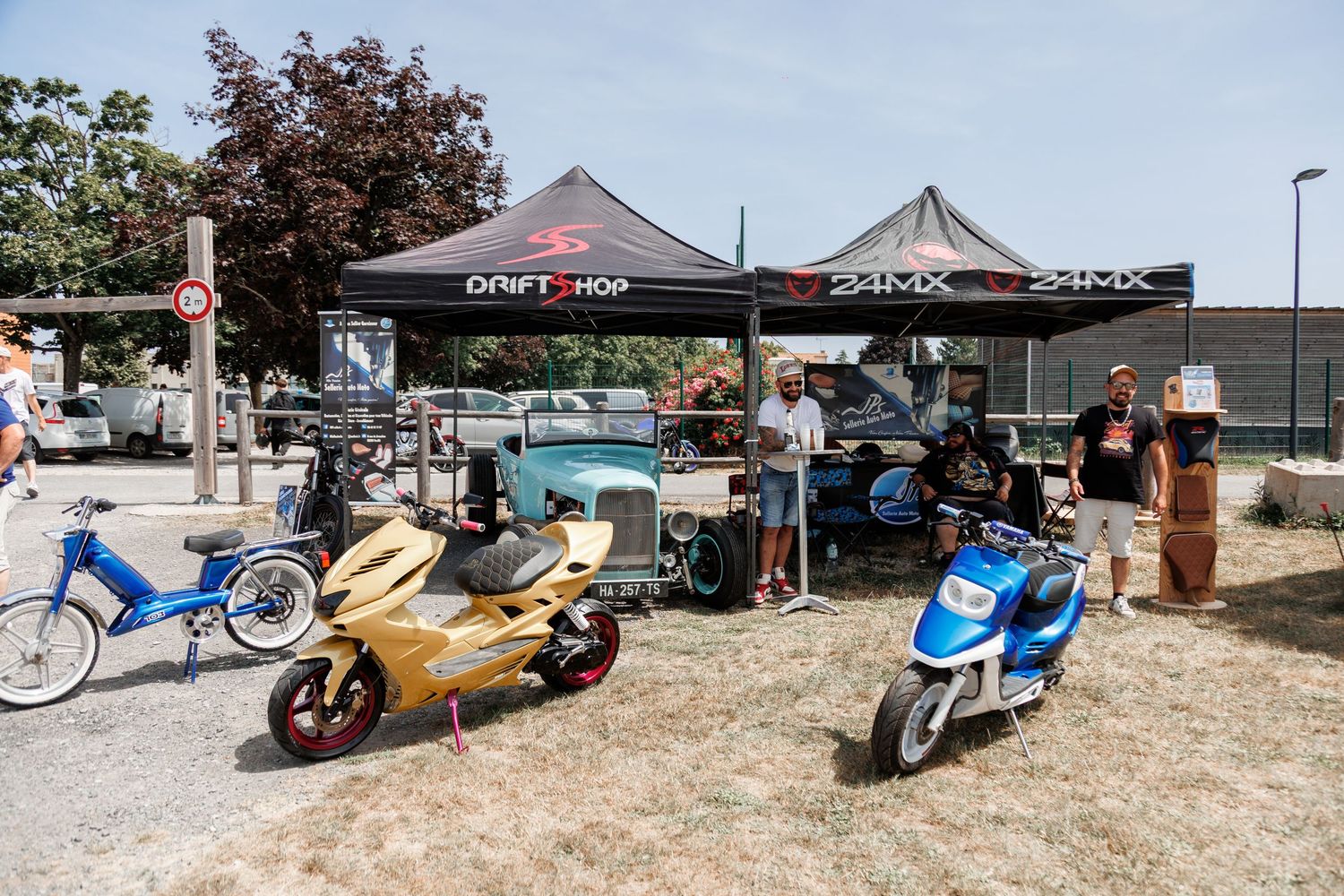 Outdoor motorsport vendor display with colorful scooters and mini bikes under black canopy tents at a sunny event.