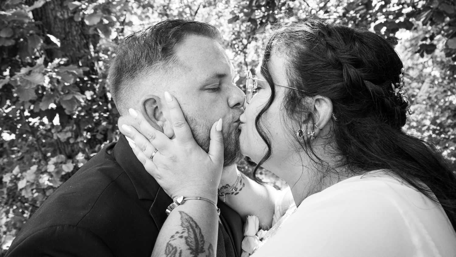 Black and white photo of tattooed groom and bride sharing a romantic kiss outdoors on wedding day.