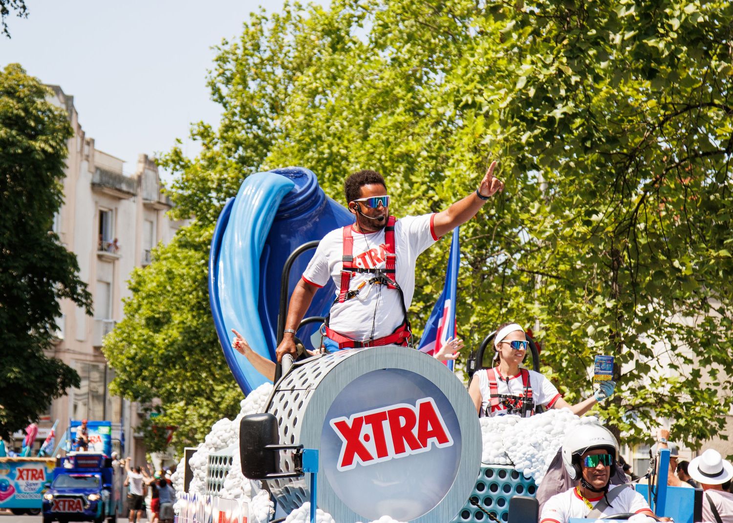 Float with XTRA branding featuring bright blue decor and performers during street festival.
