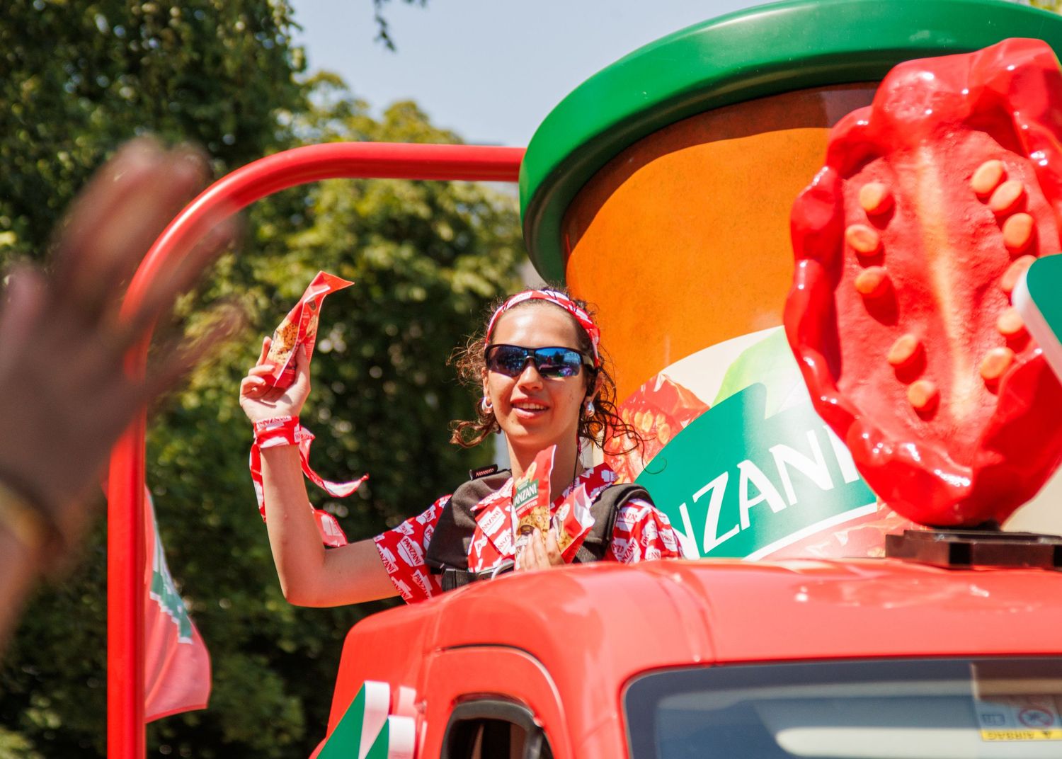 A promotional team member waves from a colorful vehicle decorated with giant food props.