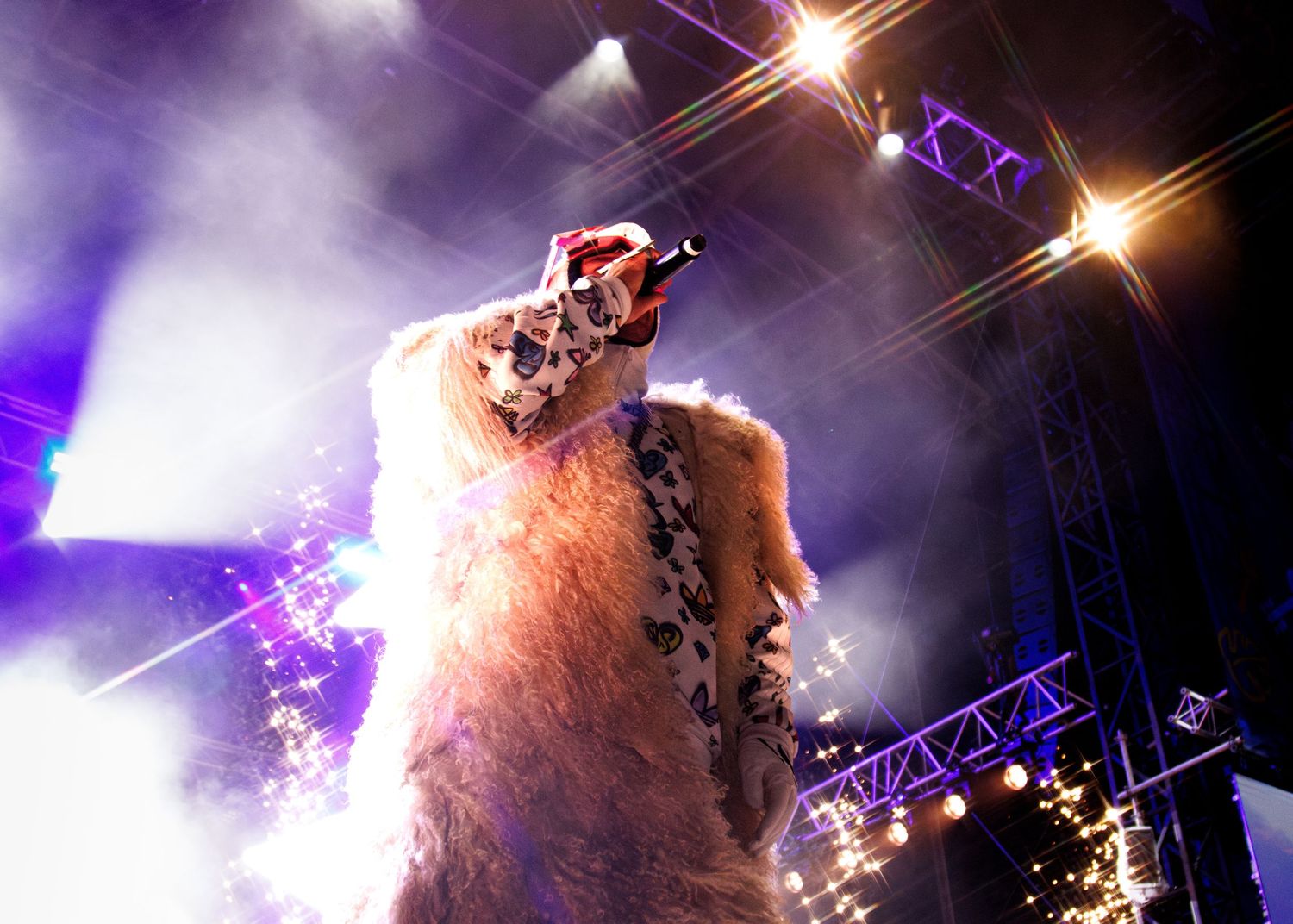 Concert performer with long hair silhouetted against dramatic purple stage lighting and fog effects during live show.