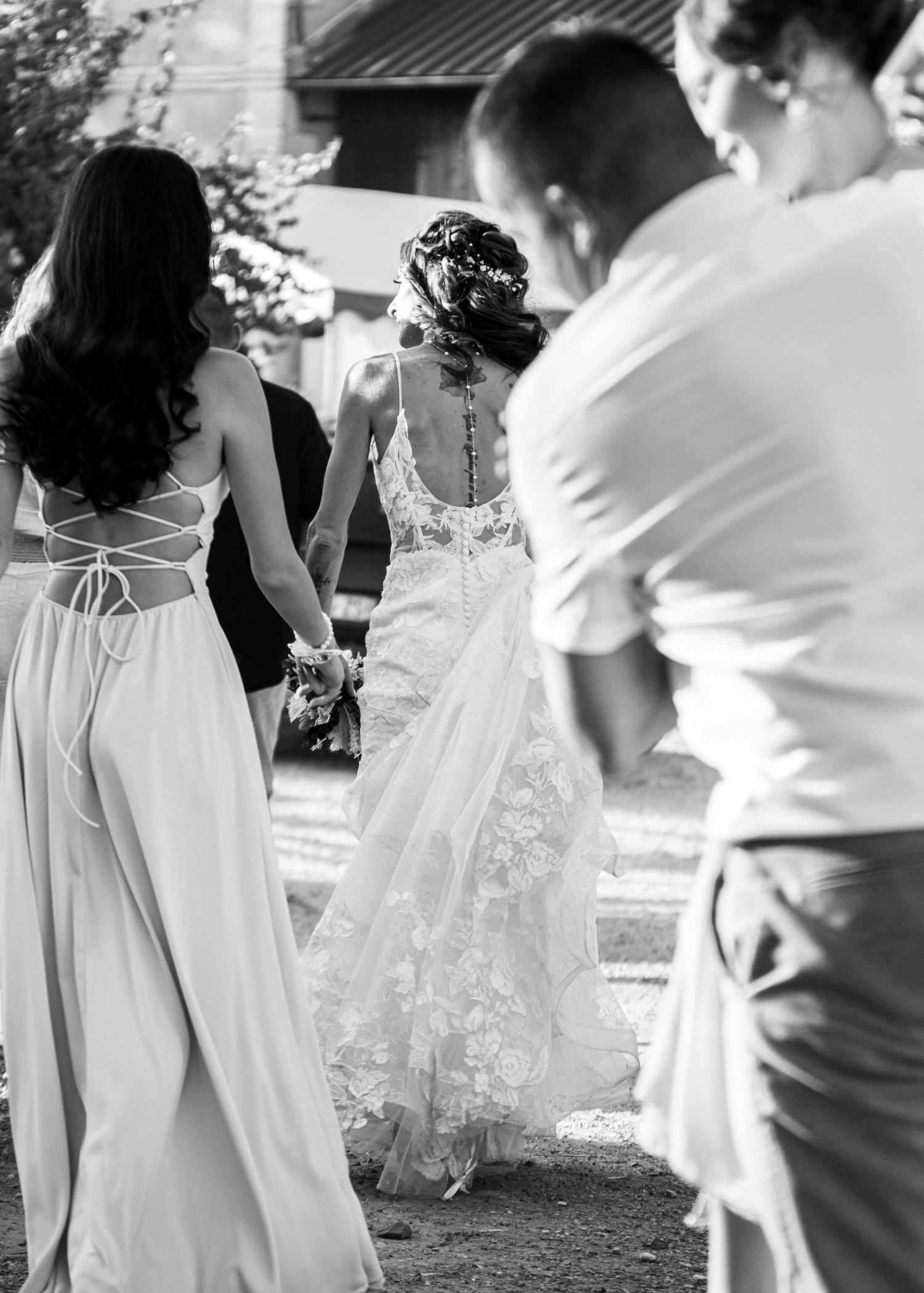 A black and white image showing three people dancing together outdoors in flowing white dresses and casual attire.