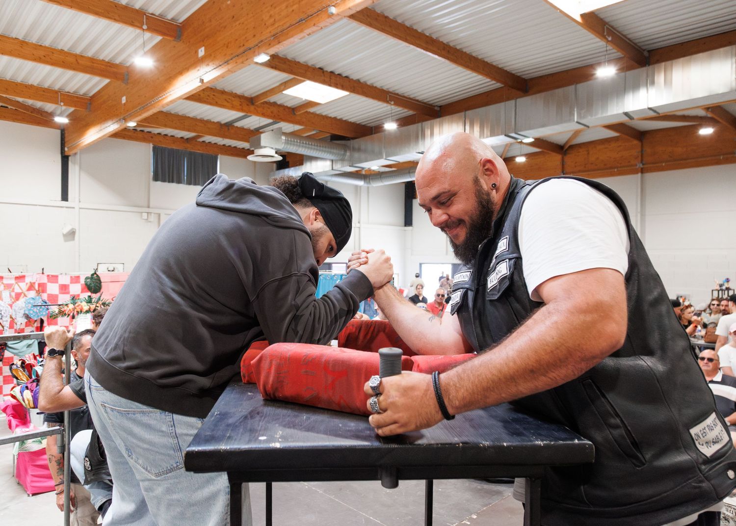 Two men arm wrestling at a table during a competitive arm wrestling tournament in a crowded indoor venue.