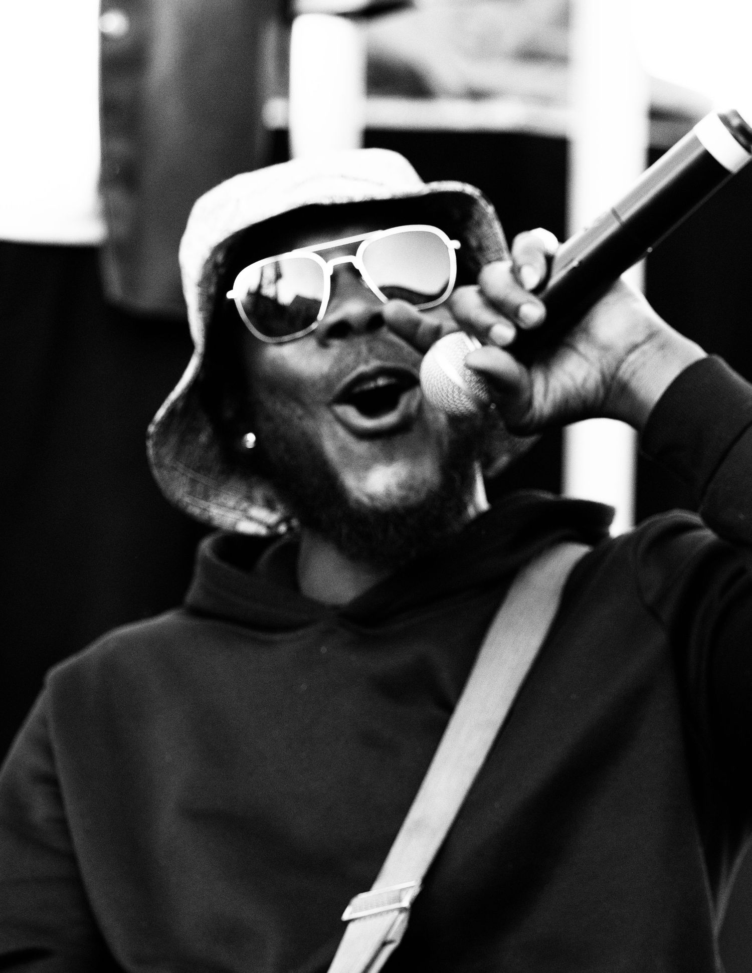 Person in bucket hat and sunglasses passionately performing with microphone.