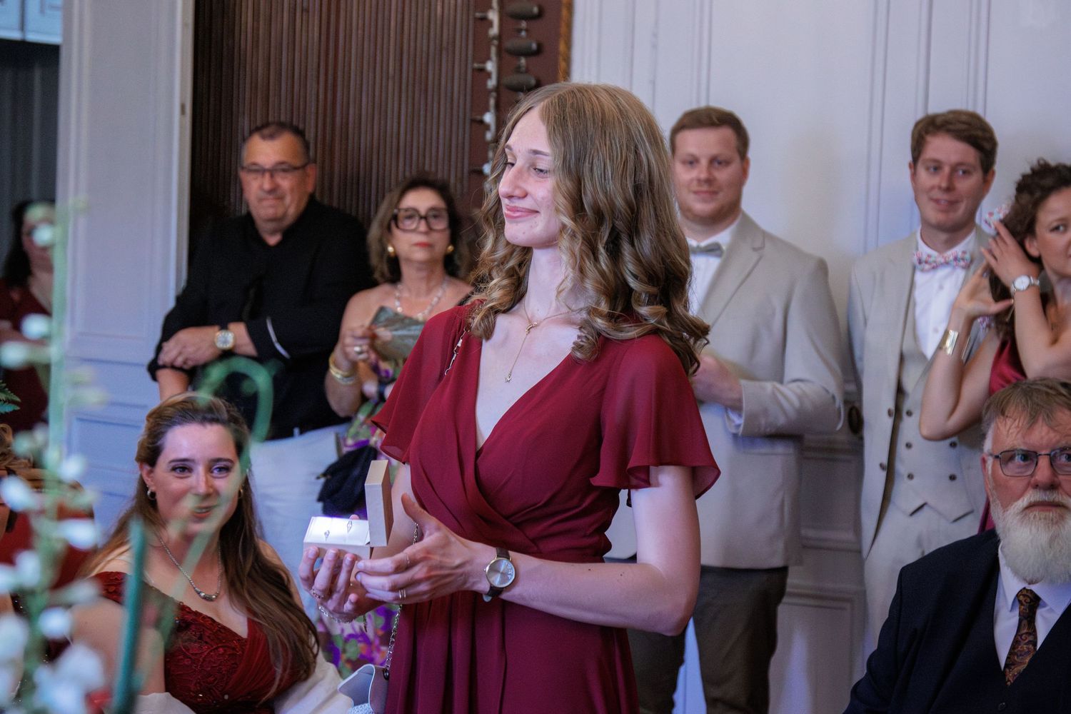 Young woman in burgundy dress smiles during an elegant indoor wedding celebration.
