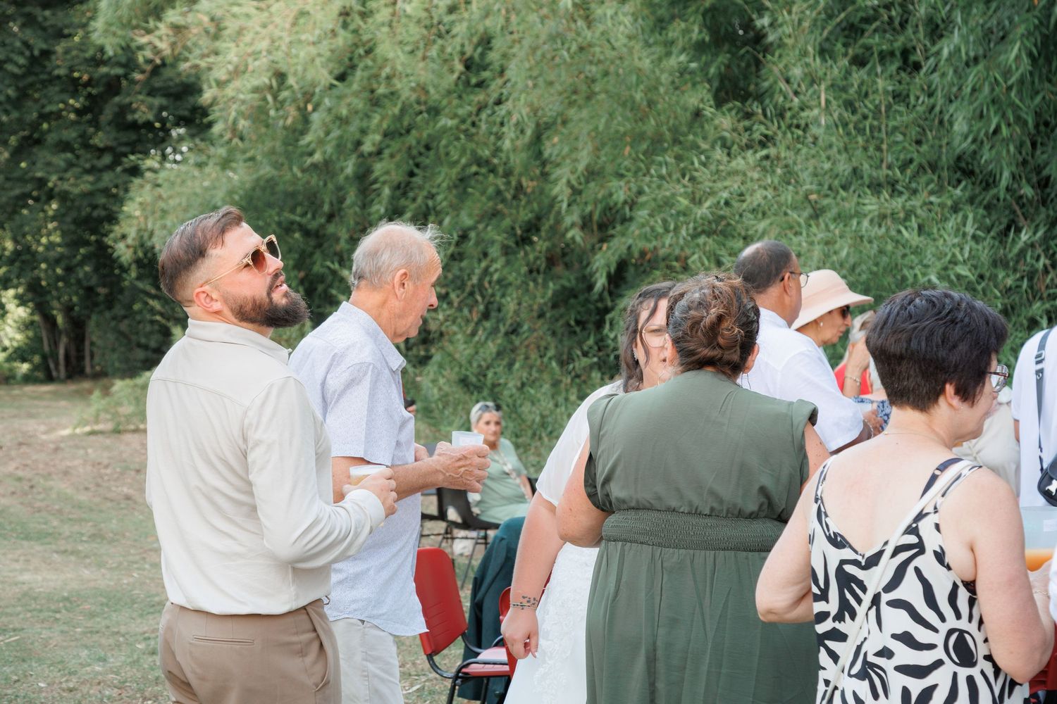 Wedding guests mingling outdoors in lush green garden setting during summer reception.