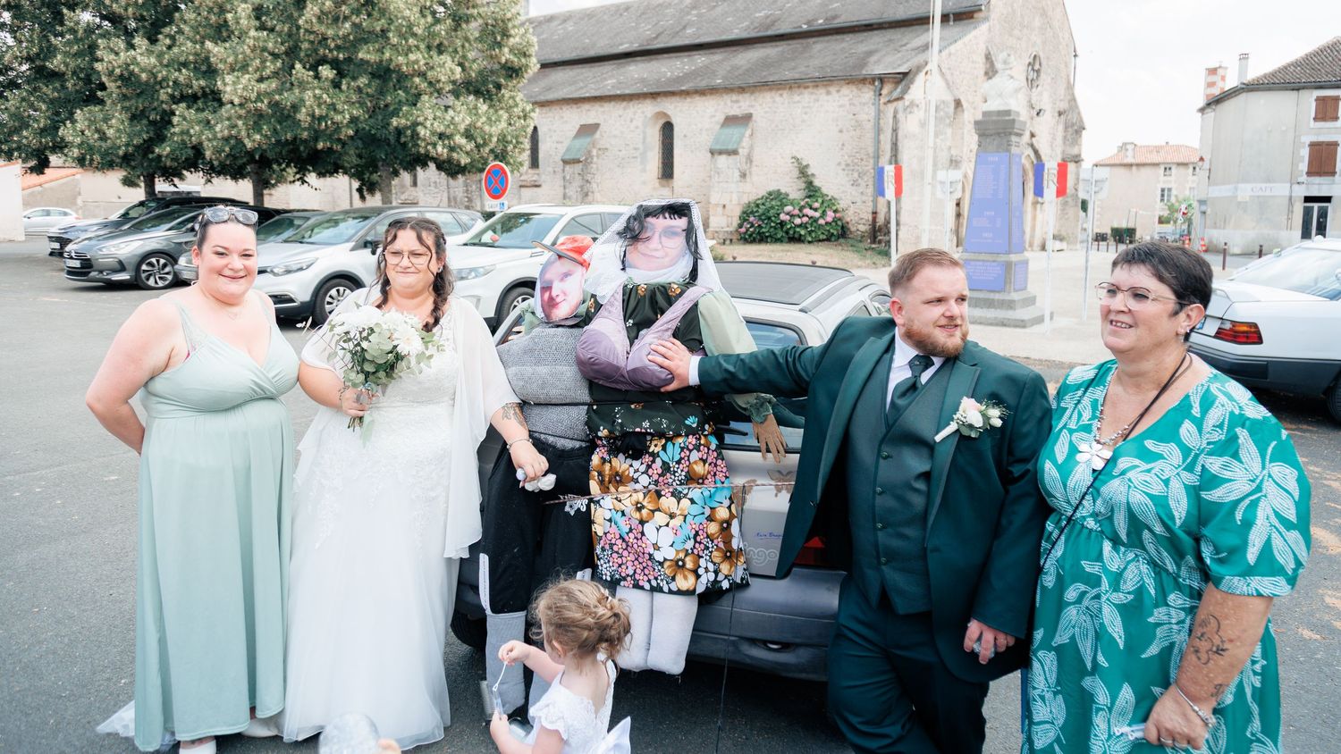 Wedding party poses beside a decorated car outside a French village square after the ceremony.