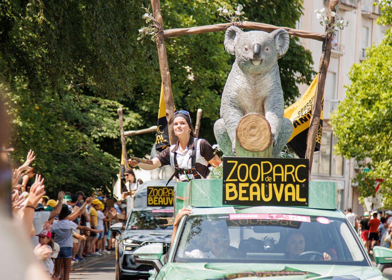 A crowd gathers along a street near a colorful zoo sign for a public event.