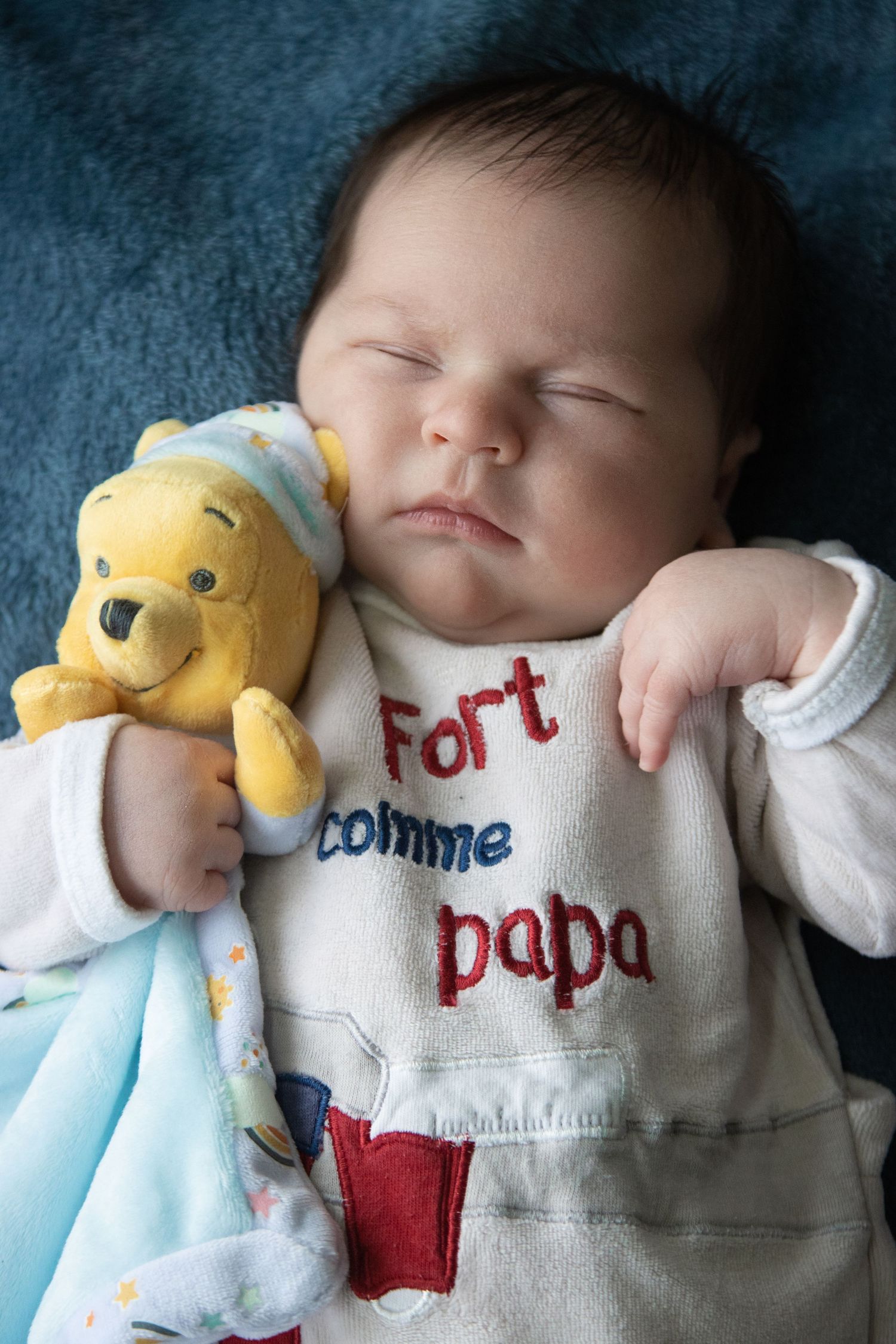 Sleeping infant cuddling yellow plush toy while wearing embroidered 'For Papa' clothing.